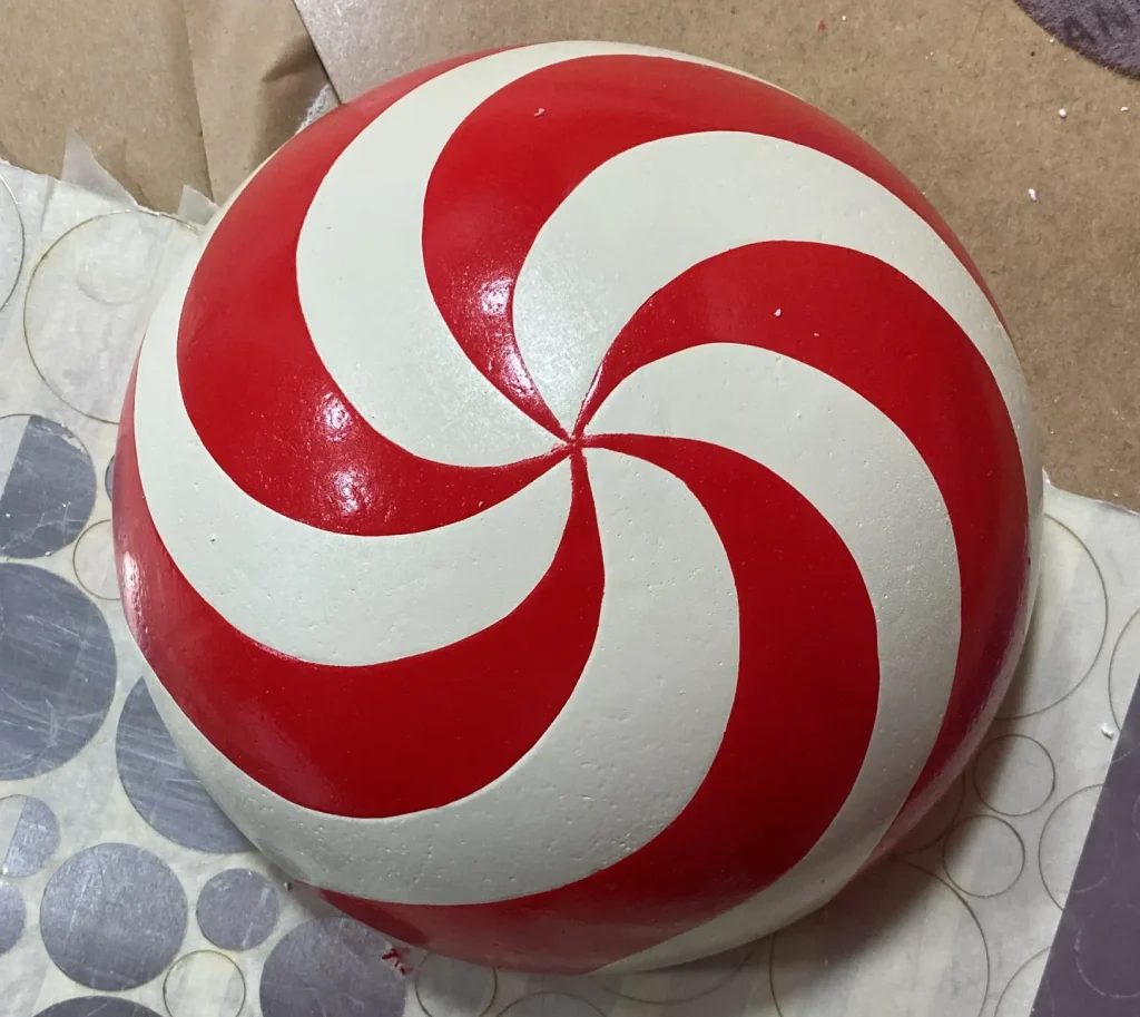 Glossy red and white peppermint swirl ornament on wrapping base