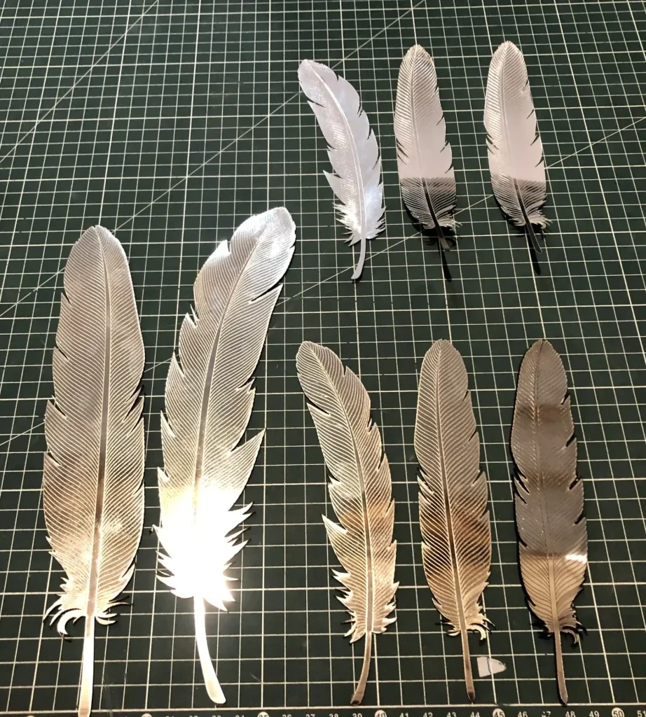 Variety of small metallic feathers laid out on green cutting mat