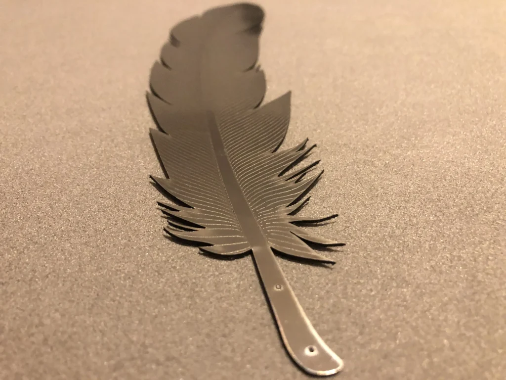 Single laser-cut metallic feather prototype on textured background