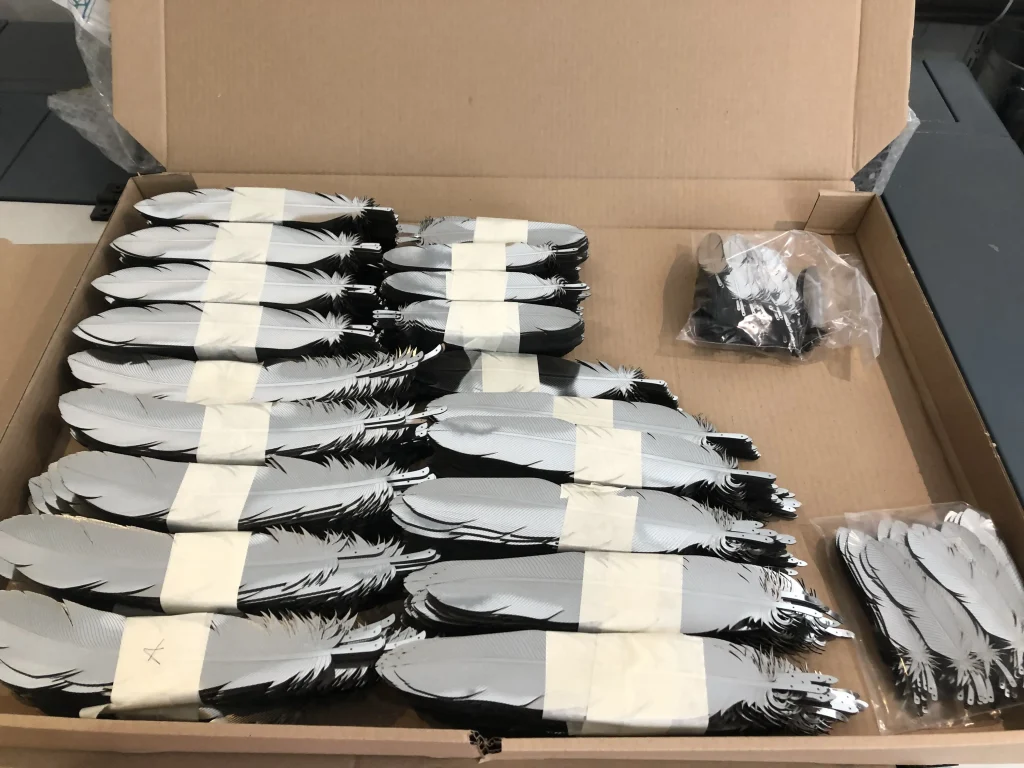 Dozens of feather prototypes stacked in box with backing adhesive